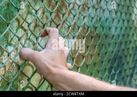 Die Hand des Mannes am Kettengliedzaun zeigt, wie sehr er durch die andere Seite gelangen will. Konzept der Freiheit Stockfoto