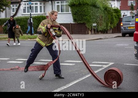 Die Feuerwehrfrau rollt den Schlauch mit der Londoner Feuerwehr aus, die an einem Hausbrand in einer Wohnstraße in South London, England, Großbritannien teilnimmt Stockfoto