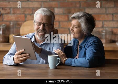Glückliche ältere Mann und Frau haben Spaß mit Tablet Stockfoto