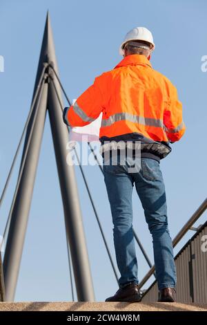 Ingenieur oder Vorarbeiter mit Hut und Arbeitsschutzkleidung Lesen Ein Plan vor industriellem Hintergrund - selektiver Fokus Stockfoto