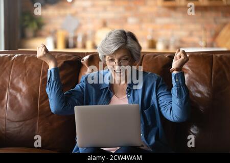 Überglücklich Senior Frau Triumph mit Nachrichten auf Laptop Stockfoto