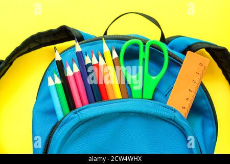 Blauer Rucksack mit verschiedenen bunten Papeterie auf gelbem Hintergrund. Zurück zur Schule Stockfoto