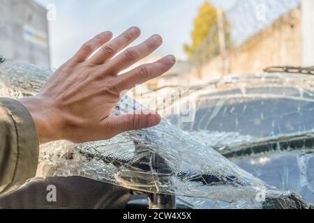 Die Faust eines Mannes gegen die zerbrochene Windschutzscheibe. Risse an der Windschutzscheibe des Fahrzeugs durch den Aufprall Stockfoto