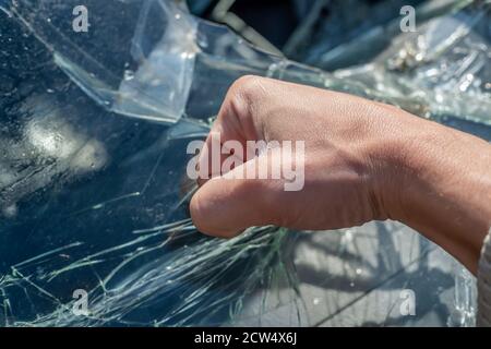 Die Faust eines Mannes gegen die zerbrochene Windschutzscheibe. Risse an der Windschutzscheibe des Fahrzeugs durch den Aufprall Stockfoto