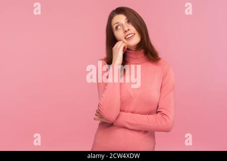 Verträumt optimistisch Brünette Frau in rosa Pullover lehnte Kopf an Hand vorstellen ihr perfektes Leben, fantasieren. Innenaufnahme des Studios isoliert auf rosa Bac Stockfoto