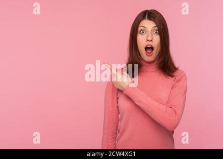 Extrem schockiert Brünette Frau in rosa Pullover zeigt weg Blick auf die Kamera mit großen Augen und offenen Mund, überrascht mit Werbung, leeren Raum Stockfoto