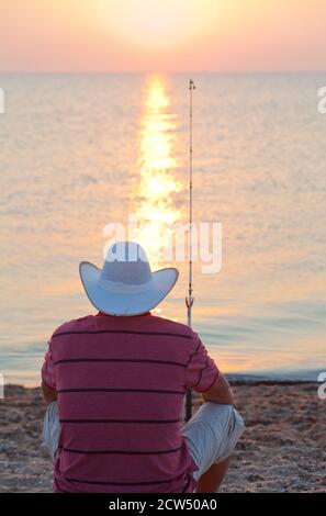 Ein Mann mit Angelrute am Ufer des Meeres, aufgehende Sonne. Stockfoto