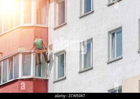 Industriekletterer versiegelt Risse in der Wand eines mehrstöckigen Gebäudes im Freien. Foto mit Beleuchtung, Licht Stockfoto