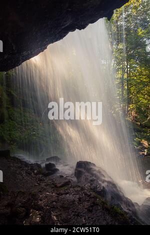 Blick von hinten auf einen malerischen Skok Wasserfall auf dem Alten Berg und golden, sonnenbeschienenen Laub der Bäume durch den Bach gesehen Stockfoto