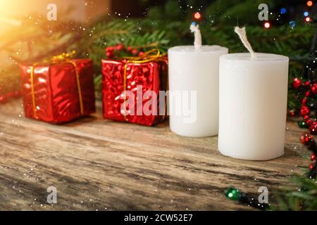 Christmas scene with white candles, red mini gifts, fir branches and garland on wooden background with copy space. Beautiful Christmas background Stockfoto