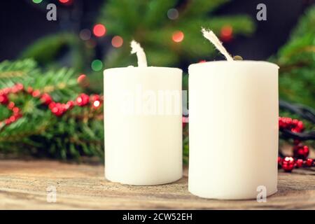 Große weiße Weihnachtskerzen auf Holzhintergrund auf Weihnachtsbaum Hintergrund mit roten Perlen Stockfoto