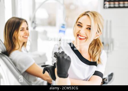 Ziemlich junge Zahnarzt hält Spritze mit Patient hinter Stockfoto