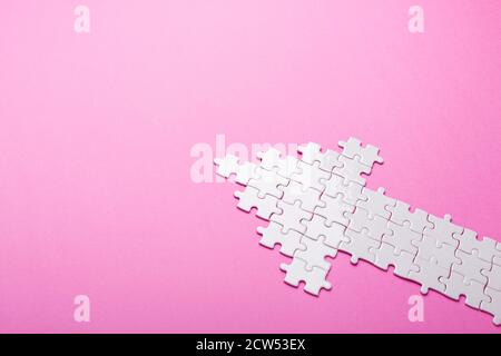 Weißes Puzzle. Pfeil Form Puzzle auf rosa Hintergrund. Draufsicht. Speicherplatz kopieren Stockfoto