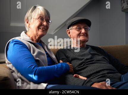 Lächelndes Senior-Paar Sitzt Auf Dem Sofa Zu Hause Fernsehen Gemeinsam Stockfoto