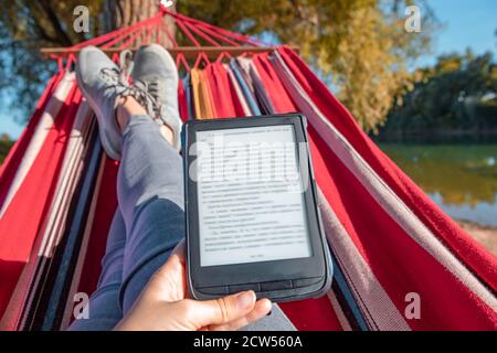 Frau, die ein Buch liest, das auf einer Hängematte im Freien am Flussstrand liegt Stockfoto