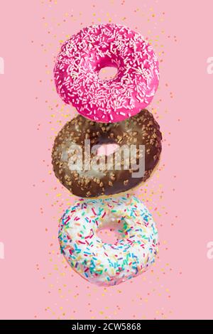 Verglaste Donuts in Bewegung fallen auf rosa Hintergrund mit bunten Streusel Stockfoto