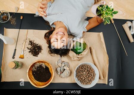 Sorglose lachende Frau, die auf dem Boden mit Gartenarbeit im Innenbereich liegt. Stockfoto