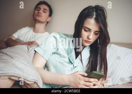 Kaukasischer Mann, der sich um seine Frau mit einer SMS-Nachricht gefreut hat Telefon, während im Bett liegend, Eifersucht zeigend Stockfoto