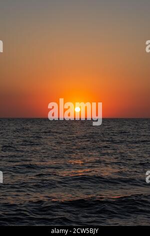 Schöner orangefarbener Sonnenuntergang über dem Meer. Die Sonne sinkt unter dem Horizont. Entspannende Meereslandschaft. Die scharlachroten Farben des Himmels und des Meerwassers. Sonnenuntergang Stockfoto