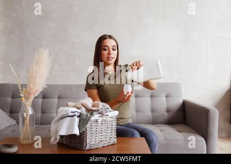 Frau gießt Waschmittel in den Flaschendeckel. Sie sitzt am Tisch mit Kleidung, die im Korb gesammelt ist Stockfoto