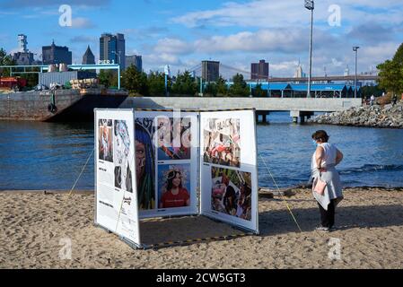 Eine Frau steht im Sand und sieht sich eine temporäre Fotoausstellung im Brooklyn Bridge Park an. Stockfoto