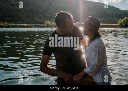 Mann und Frau stehen in einem See lächelnd und reden An einem sonnigen Tag Stockfoto