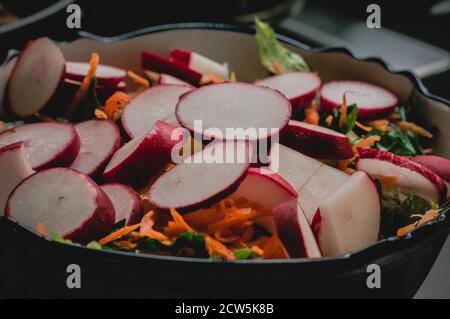 Bunte Salatschüssel mit Rettich, geriebener Karotte und Salat Stockfoto