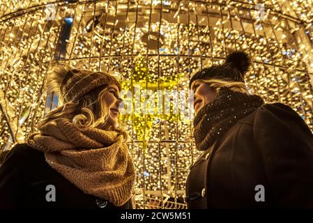 Zwei junge Mädchen lachen im Hintergrund der weihnachtsbeleuchtung. Stockfoto