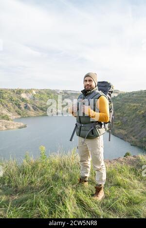 Glücklicher junger bärtiger Tourist mit Rucksack, der oben auf steht Berg Stockfoto