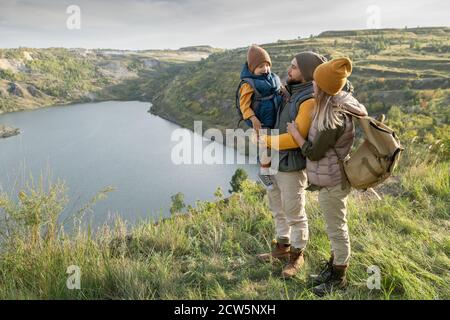 Junge Eltern und ihr kleiner Sohn mit Rucksäcken, gegen die sie stehen see oder Fluss Stockfoto