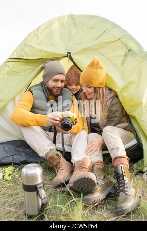 Junger Mann zeigt Fotos in Fotokamera zu seinem Sohn und Ehefrau in Ruhe Stockfoto