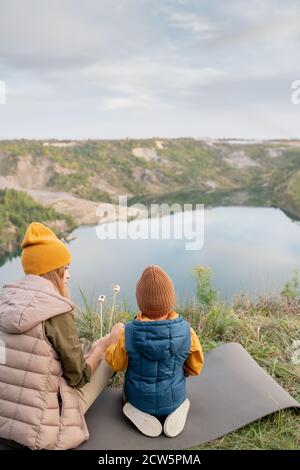 Rückansicht von jungen zeitgenössischen Backpacker und kleinen Jungen Auf dem Teppich sitzend Stockfoto