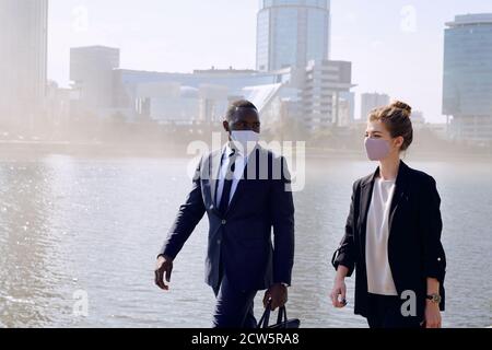 Zwei Geschäftspartner in formalwear und Schutzmasken ziehen an riverside Stockfoto