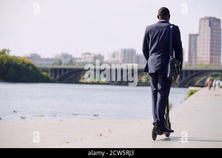 Rückansicht des jungen eleganten Geschäftsmannes in formalwear, der weiter geht Elektroroller Stockfoto