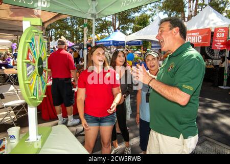 Ein katholischer Diakon gesellt sich mit jungen Gemeindemitgliedern an einem Rad des Zufalls während einer überdachten Straßenmesse Outreach-Ausstellung in Laguna Niguel, CA. Stockfoto