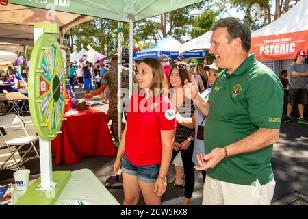 Ein katholischer Diakon gesellt sich mit jungen Gemeindemitgliedern an einem Rad des Zufalls während einer überdachten Straßenmesse Outreach-Ausstellung in Laguna Niguel, CA. Stockfoto