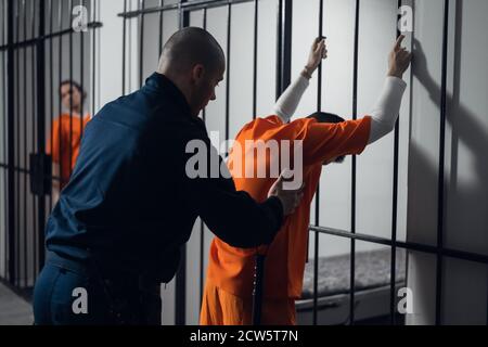 Eine bewaffnete Wache durchsucht einen neu angekommenen Verbrecher in einem Gefängniskorridor vor dem Hintergrund von Bars Stockfoto