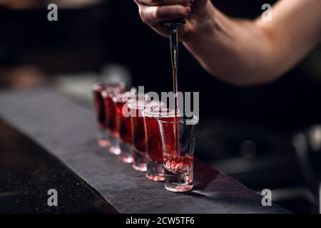 Der Barkeeper füllt seine Schüsse mit rotem Schnaps aus einer Flasche an der Bar. Stockfoto