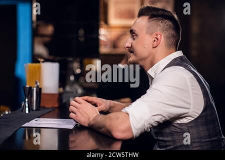 Ein junger Mann in Hemd und Weste bestellt von der Speisekarte an der Bar. Stockfoto