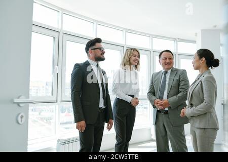 Fröhliche interkulturelle Kollegen schauen auf junge elegante Geschäftsfrau Stockfoto