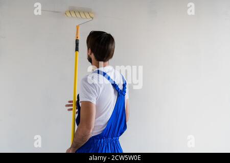 Die Werkstatt in der Arbeitskleidung malt die Wand weiß mit einem Rolle Stockfoto