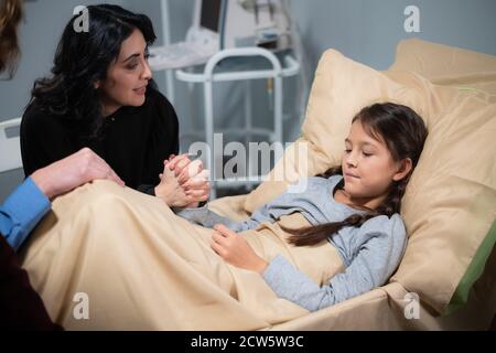 Als liebevolle Mutter am Bett ihrer Töchter liegt das Mädchen in einem Krankenhausbett. Stockfoto