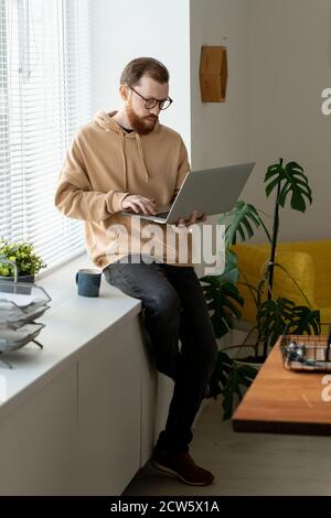 Junge seriöse Freiberufler mit Laptop, Kaffee und Remote-Arbeit Stockfoto