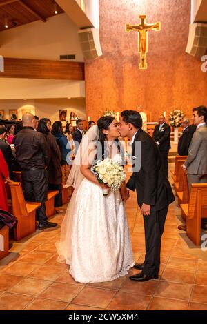 Eine gerade verheiratete Braut und ein Bräutigam küssen im Gang einer katholischen Kirche in Südkalifornien. Stockfoto