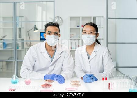 Zwei junge interkulturelle Kliniker in Whitecoats, Schutzmasken und Handschuhen Stockfoto