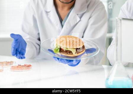 Handschuhen der männlichen Arbeiter der Lebensmittelqualitätskontrolle halten Teller mit Hamburger Stockfoto