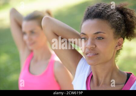 Zwei hübsche Frauen, die sich vor dem Training in einem Park strecken Stockfoto