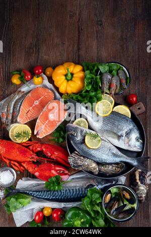 Frischer Fisch und Meeresfrüchte mit Kräutern, Gewürzen und Gemüse auf rustikalem Holzhintergrund. Ausgewogene Ernährung und Kochkonzept. Gesunde Ernährung. Draufsicht mit Stockfoto