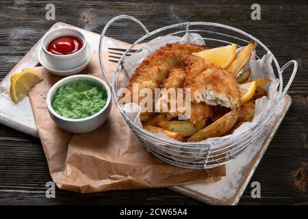 Britische traditionelle Küche Fisch und Chips. Serviert mit pürierten Erbsen und verschiedenen Saucen. Stockfoto