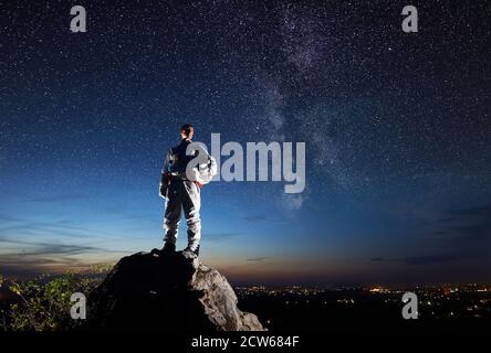Weltraumreisender, der auf einem felsigen Hügel steht und den wunderschönen Himmel mit Sternen betrachtet. Astronaut im weißen Raumanzug mit Helm. Konzept der Raumfahrt und Kosmonauten. Stockfoto